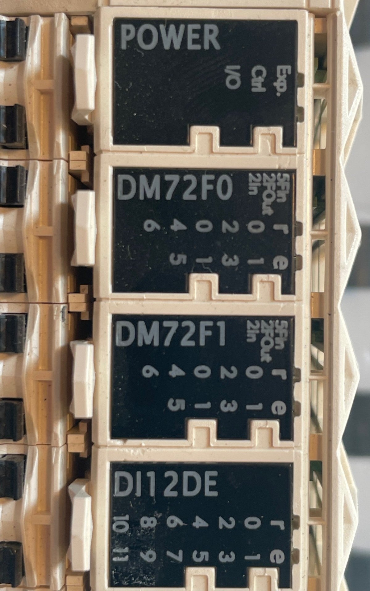 A close-up of industrial electrical relays, featuring black labels with white text for POWER, DM72F0, DM72F1, and DI12DE, mounted in a beige plastic housing. Schneider Electric TM258LD42DT Modicon M258 complete PLC and I/O module assembly
