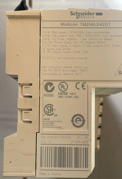 Close-up of a Schneider Electric Modicon TM258LD42DT electrical module showing technical specifications and certification labels on its beige plastic housing.