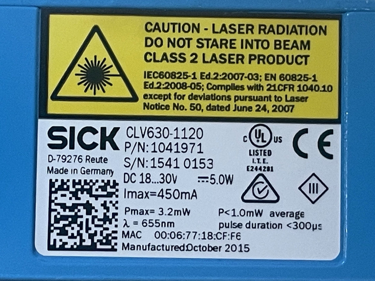 Close-up of a blue laser enclosure with a white and yellow product label. The label shows the brand SICK, model CLV630-1120, class 2 laser product warning, technical specifications, a QR code, and certification marks including UL and CE.