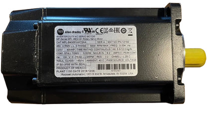 An Allen-Bradley industrial servo motor, model MFR 480V AC Servo Motor, shown from a top-down angle on a wooden surface. The motor has a black plastic housing with a white technical specification label in the center and a yellow shaft visible on the right.