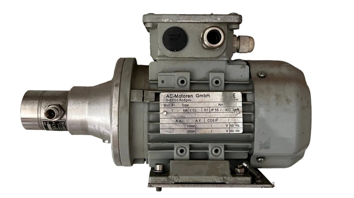 An industrial electric motor with a gray cast metal housing and a silver metallic shaft, resting on a textured gray concrete floor. 