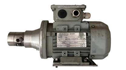 An industrial electric motor with a gray cast metal housing and a silver metallic shaft, resting on a textured gray concrete floor. 