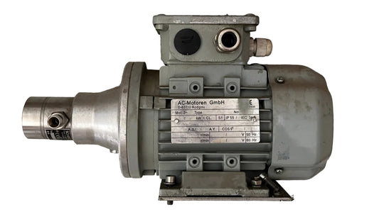 An industrial electric motor with a gray cast metal housing and a silver metallic shaft, resting on a textured gray concrete floor. 